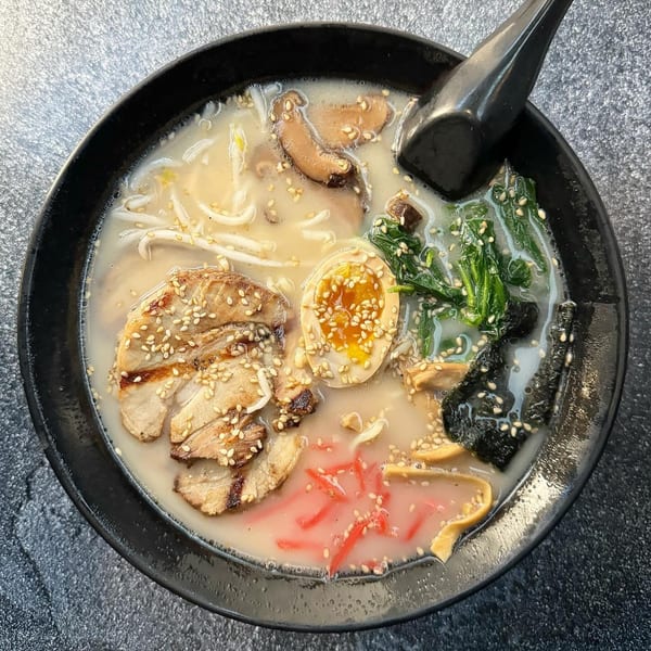 A close-up of a Banzai Sushi ramen bowl with pork, egg, mushrooms, spinach, and red ginger.