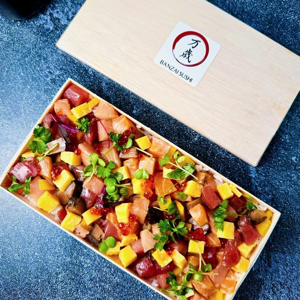 A Banzai Sushi chirashi bowl with colorful diced fish, egg, and greens in a wooden box.
