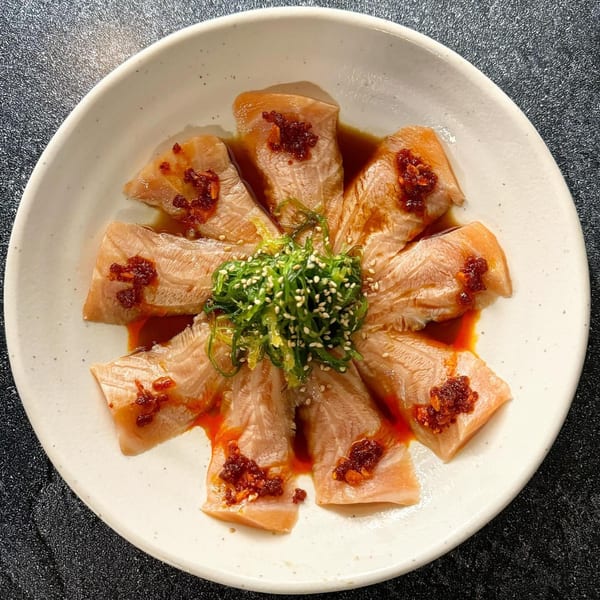 Banzai Sushi's salmon sashimi with chili oil, green onions, and sesame seeds on a white plate.